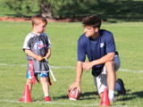 High Schooler boy teaching a young boy flag football