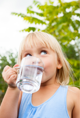 Small blond child drinking water in a clear, glass mug outside
