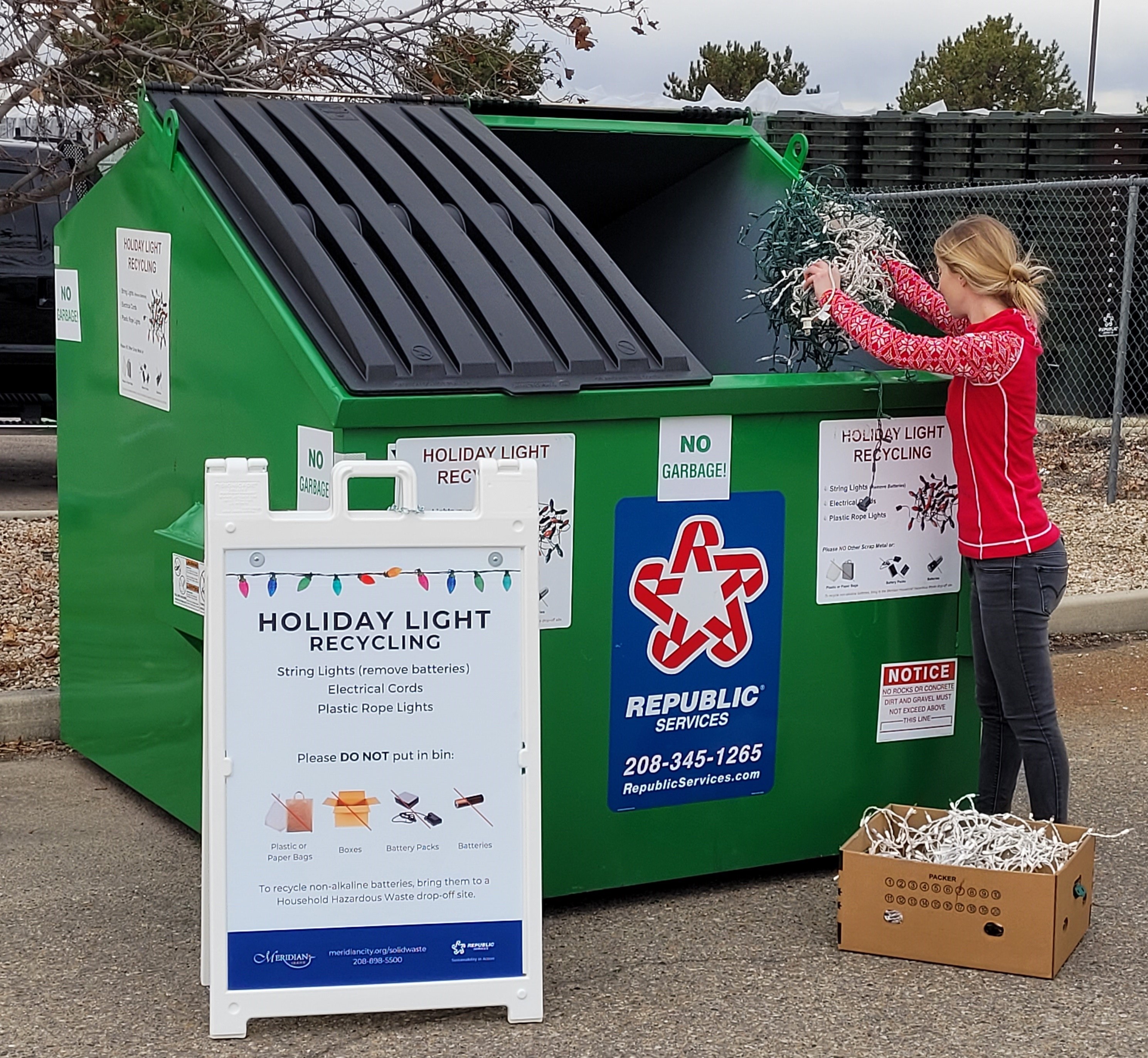 Person with a box of old holiday lights, placing strands into the Holiday Light Recycling bin